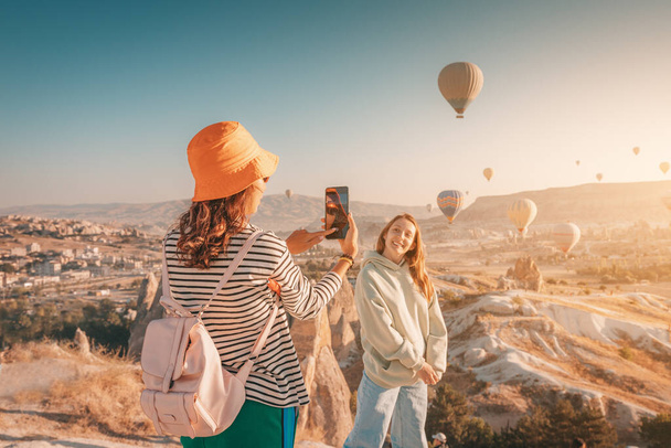 Two happy girl friends taking photos and video on phone for social networks in Cappadocia, Turkey. Travel and influencer concept - Photo, Image