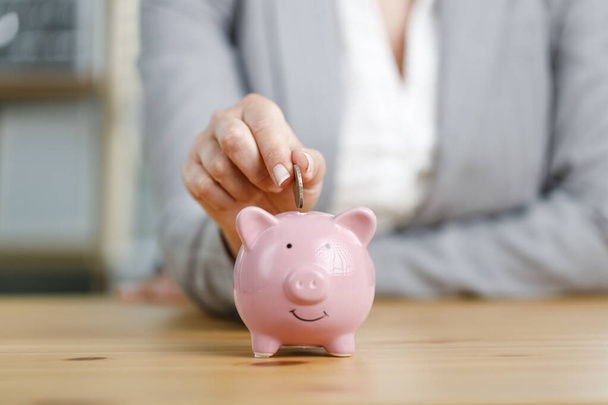 Businesswoman putting money into piggy bank. Concept of money saving and budgeting. Saving money with pink cute piggy bank - Photo, Image