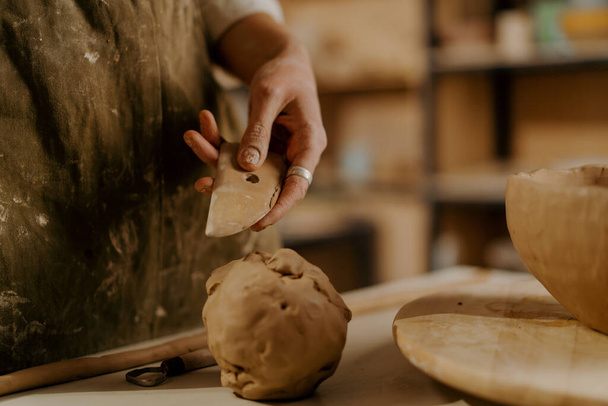 Pottenbakkerswerkplaats, een werktuig voor het verwerken van klei in de handen van meesterklei ligt op tafel - Foto, afbeelding