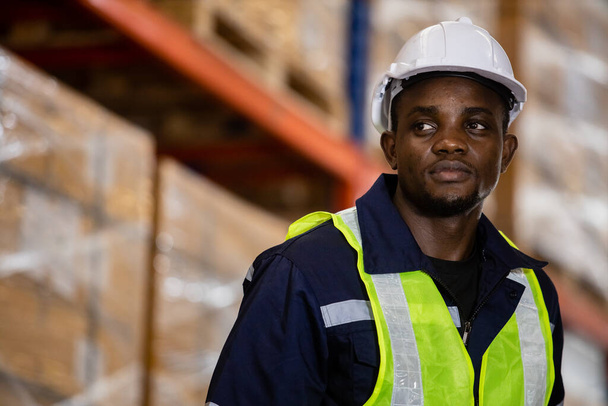 Egy afro-amerikai munkás, aki biztonsági egyenruhát és keménykalapot visel a raktárban. üzleti logisztika és szállítás. - Fotó, kép