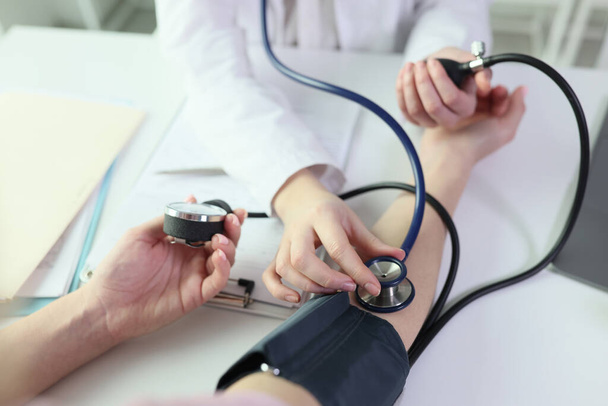 Doctor measures patients blood pressure using sphygmomanometer and stethoscope. Close-up of process of measuring blood pressure. - Photo, image