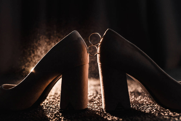 gold wedding rings on a dark background with reflection of wedding shoes light splashing water. High quality photo - Foto, imagen