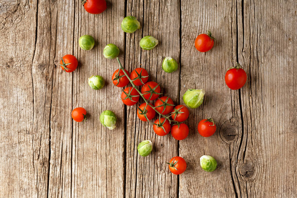 Small cherry tomatoes and Brussels sprouts on an aged wooden background. Mix of fresh healthy vegetables. A symbol of proper, wholesome nutrition. - Zdjęcie, obraz