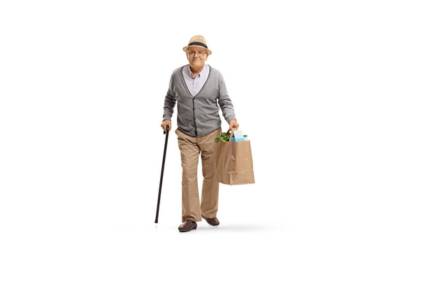 Full length portrait of an elderly man with a cane walking and carrying a paper grocery bag isolated on white background - Photo, Image