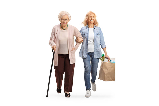 Full length portrait of a woman helping an elderly lady and carrying grocery bags isolated on white background - Photo, Image