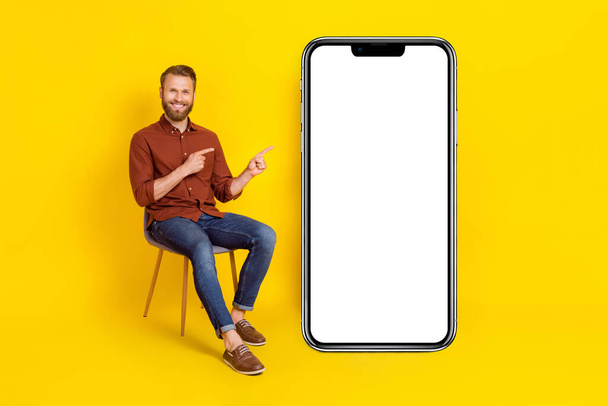 Full length portrait of handsome guy sit chair indicate fingers empty space isolated on yellow color background. - Fotoğraf, Görsel
