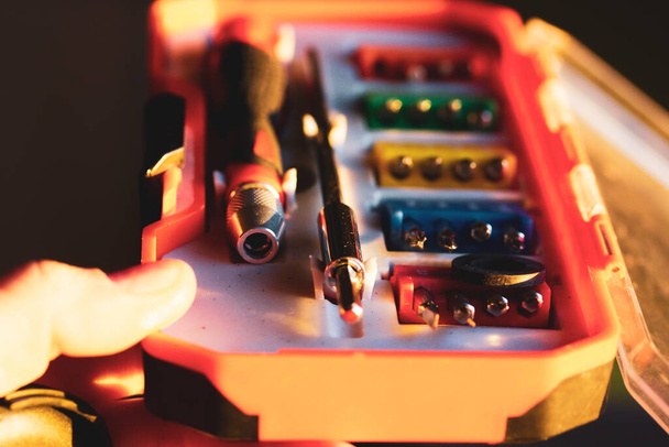 Um conjunto de várias chaves de fenda bits com diferentes anexos em uma caixa de plástico laranja em uma mão mestra. Chave de fenda diferente para o trabalho de reparação. Conjunto de ferramentas para pequenos reparos. Conjunto de ponta de chave de fenda. - Foto, Imagem