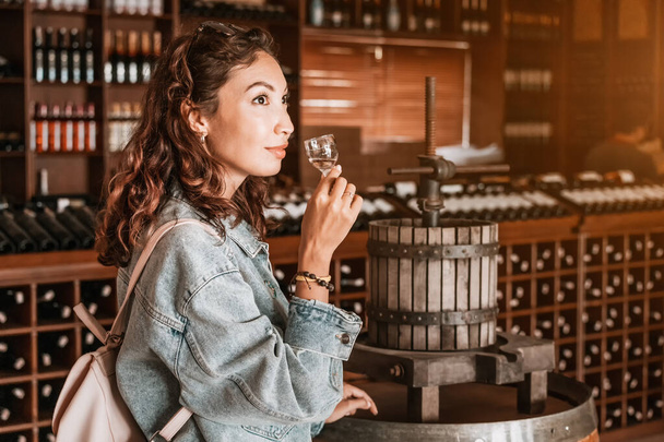 A contented female visitor to a winery pauses to enjoy a sip of a refreshing white wine. - Fotografie, Obrázek