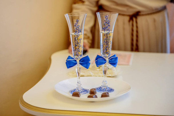 Twee glazen champagne met blauwe strikken op een dienblad bonbons. - Foto, afbeelding