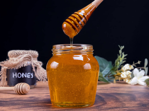 Medová lžička vychází ze sklenice plné medu ve zpomaleném filmu. Med obsahuje mnoho živin, antioxidanty, zlepšuje zdraví srdce, péče o rány, nabízí antidepresiva a anti-úzkost výhody - Fotografie, Obrázek