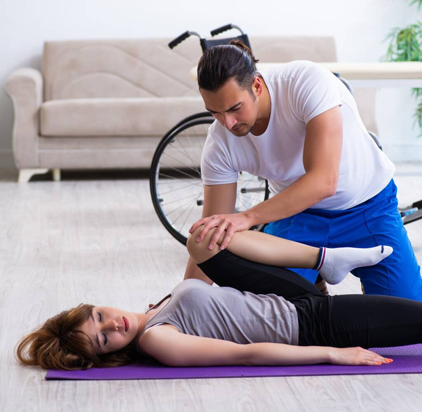 Мужчина-физиотерапевт делает упражнения с травмированной женщиной на полу - Фото, изображение