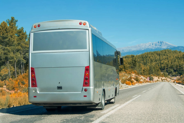 Silver shiny gray modern comfortable tourist bus driving through highway at bright sunny day mountains. Travel and coach tourism concept. Trip and journey by vehicle - Foto, Imagem