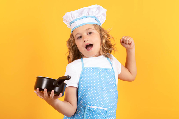 Funny kid chef cook with kitchen pot stockpot. Cooking, culinary and kids. Little boy in chefs hat and apron on studio isolated background - Фото, изображение