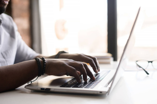 Mannelijke handen op het toetsenbord van de laptop. man afrikaans-amerikaanse kantoor werknemer in casual shirt werken met laptop computer, gezicht is niet zichtbaar - Foto, afbeelding