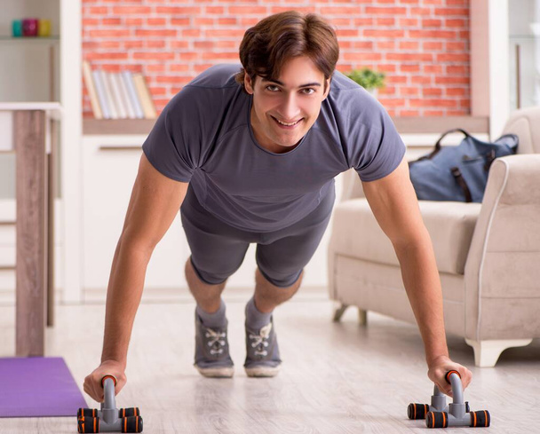 El joven guapo haciendo ejercicios deportivos en casa - Foto, imagen