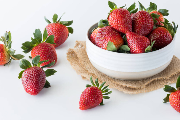 A bowl full of ripe juicy strawberries with several scattered about on the table. - Photo, Image