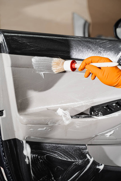 Araba temizleme servisi. Temizlik işçisi, müşterilerin iç çamaşırlarını yıkıyor. Araba kapısı paneliyle köpük ve deterjan temizleme işlemi - Fotoğraf, Görsel