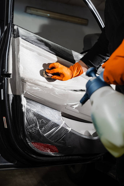 Proces czyszczenia pędzlem guzików samochodu pianką i detergentem panelu karty drzwi samochodu. Usługa detalowania samochodu. Pracownik sprzątający mycie wnętrz klientów auto - Zdjęcie, obraz