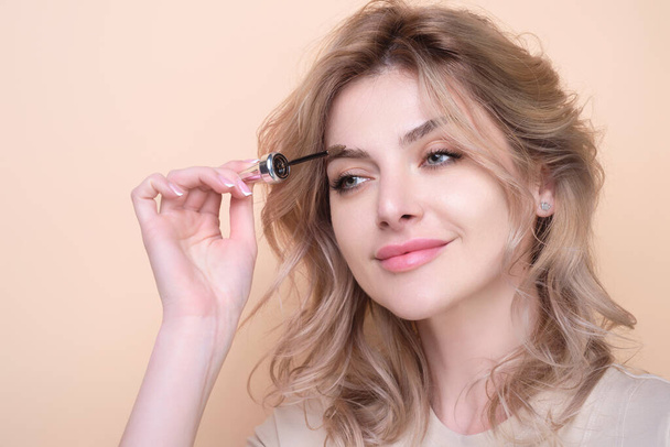 Beautiful woman applies brow gel with brows brush to her eyebrow. Studio portrait of young woman doing her eyebrow natural make up. Eyebrows make up concept - Foto, Imagem