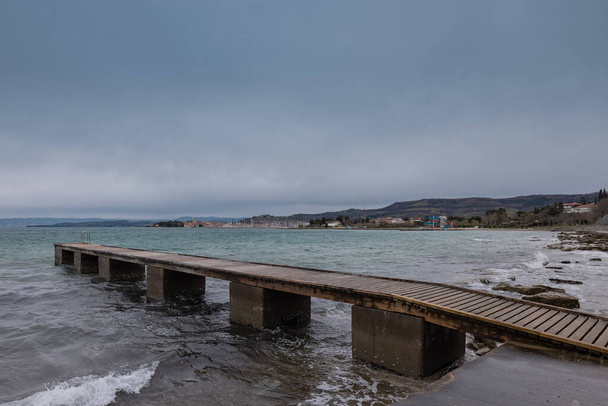 View of a pier in Izola below Bellevedere viewpoint on the north of Adriatic coast. Cloudy weather and long pier. Izola in the background - Photo, Image