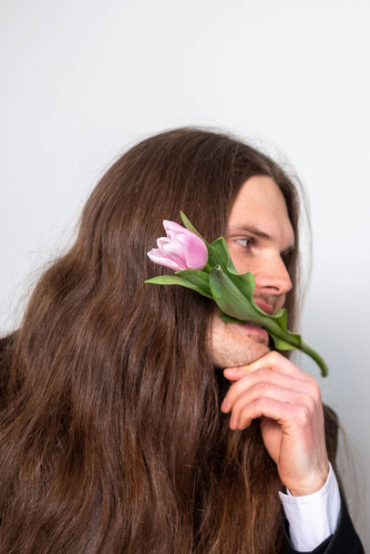 Красивый мужчина с длинными каштановыми волосами, держащий тюльпан во рту. - Фото, изображение