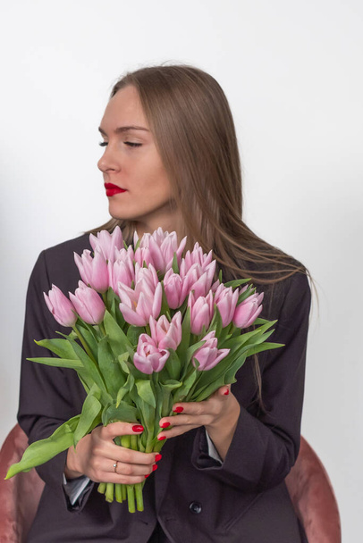 Beautiful woman in a suit holding a pink bouquet of tulips. Seri - Photo, Image