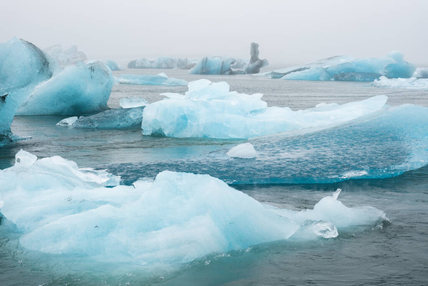 Big Blue Icebergs in Jokulsarlon Glacier Lagoon. Glacial Drift at Calm Water. Pure Ice Chunks from Melting Glacier. Icy Winter Landscape. Foggy Weather in Iceland. High quality photo - Fotó, kép