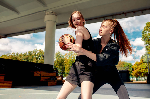Two young women playing basketball on street court on a sunny day. Women playing a streetball game outdoors - Photo, Image