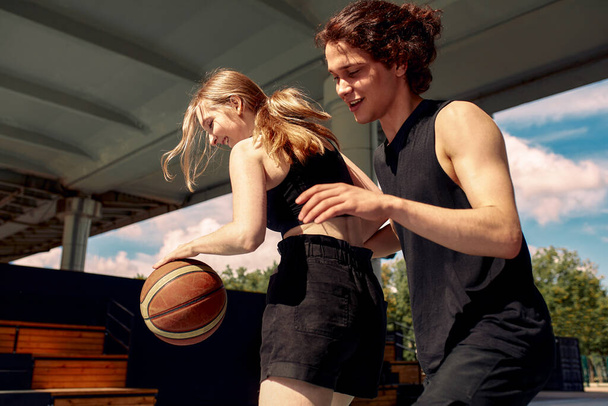 Молоді люди грають у баскетбол на вулиці, дівчина і хлопець грають у стрітбол на міському майданчику
. - Фото, зображення