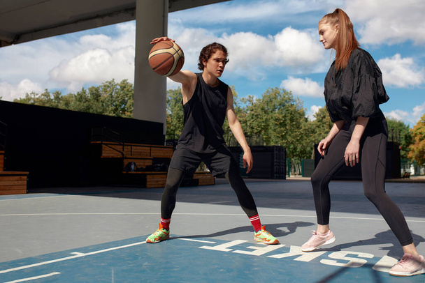 Молодые люди играют в баскетбол на улице, девушка и парень играют в стритбол на городской площадке. - Фото, изображение
