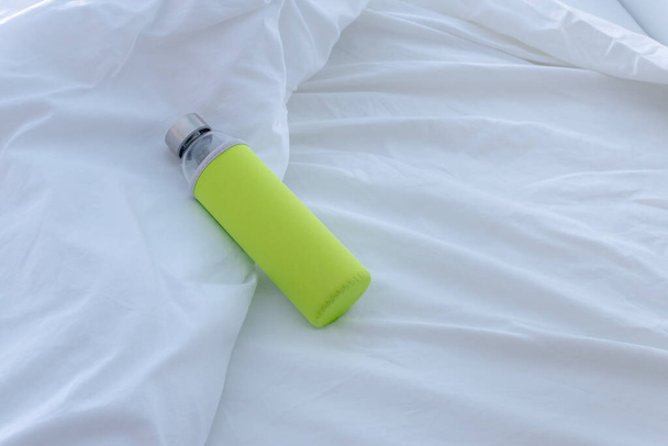 Stylish Glass Water Bottle with Colorful Sleeve on White Bed Linens - Φωτογραφία, εικόνα