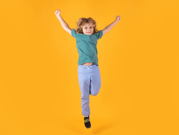 Energetic kid boy jumping and raising hands up on isolated studio background. Full length body size photo of jumping high child boy, hurrying up running fast on yellow background - Photo, image