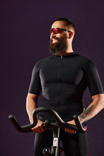 Férfi mosolygós edzés kerékpár sötét háttér, ember csinál kardió edzés a testmozgás kerékpár, zsírégetés, fogyás, sport életmód koncepció. - Fotó, kép