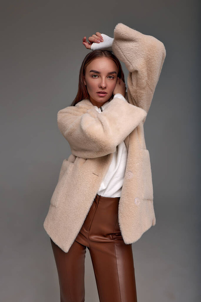 Beautiful fashionable woman in a cozy fur coat on a gray background positive girl posing at the camera in beautiful spring clothes. - Photo, Image
