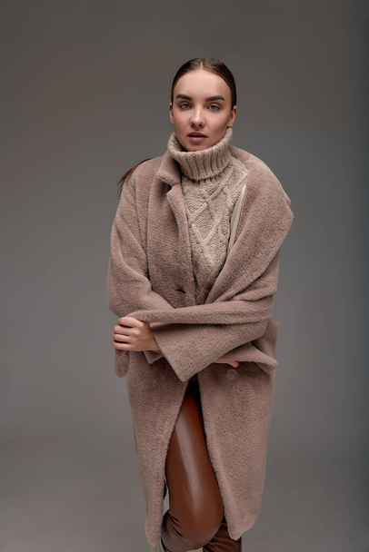 Fashion jonge vrouw in een faux fur jas op een grijze achtergrond - Foto, afbeelding