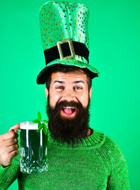 Szczęśliwy brodaty mężczyzna w karłowatym kapeluszu pijący piwo w pubie lub barze. Święto Św. Patryka. Uśmiechnięty człowiek ze szklanką zielonego piwa. Zielony napój z koniczyną. Święto Św. Patryka lub święto oktoberfest - Zdjęcie, obraz