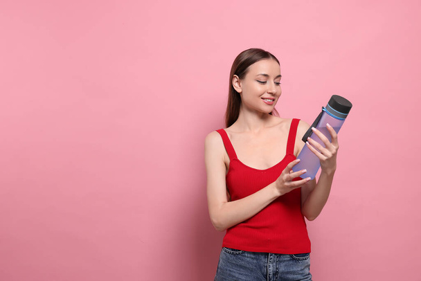 Beautiful young woman with transparent bottle on pink background, space for text - Photo, image