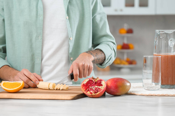Man preparing ingredients for tasty smoothie at white marble table in kitchen, closeup - Photo, Image