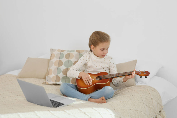 Little girl learning to play ukulele with online music course at home. Space for text - Foto, Bild