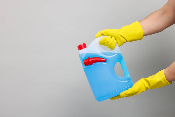 Man in rubber gloves holding canister with blue liquid on light grey background, closeup. Space for text - Photo, Image