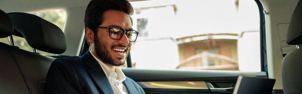 Усміхнений бізнесмен у костюмі робочого ноутбука під час їзди в машині до офісу. Високоякісна фотографія
 - Фото, зображення