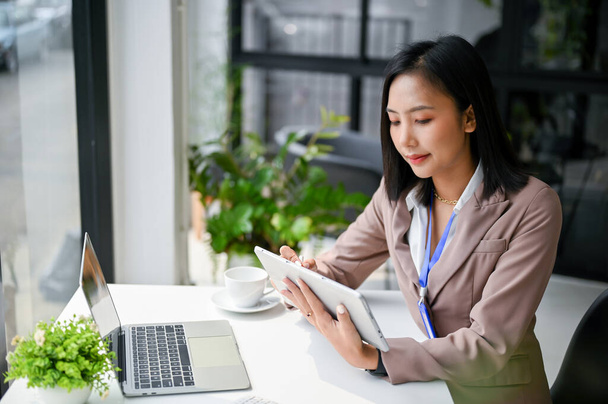 Vonzó gyönyörű millenniumi ázsiai üzletasszony vagy női bankár használja a táblagépét az íróasztalánál az irodában. technológia és üzleti koncepció - Fotó, kép
