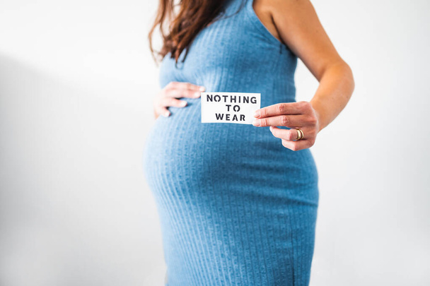 Nothing to Wear sign held by pregnant woman in the last month of pregnancy wearing stretchy blue dress showing her bump, maternity wear and inclusive fashion concept - Foto, Bild