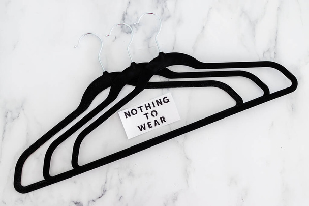 fashion and shopping concept, Nothing To Wear text on group of empty clothes hangers creating geometric shape on marble background - Photo, Image