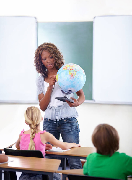 Learning about the continents. A young teacher showing her class a globe of the world during geography - Foto, immagini
