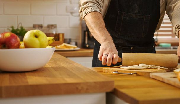 Hände in Großaufnahme Mann mit Schürze hält Nudelholz, Teig auf Küchentisch. - Foto, Bild