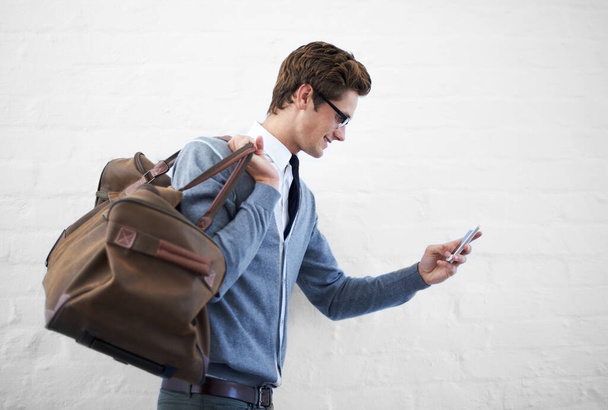 En marcha y en contacto. Un joven empollón en movimiento con una bolsa y su teléfono - Foto, Imagen