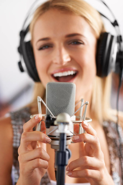 Following her dreams, one song at a time. A closeup of a beautiful blonde woman singing into a microphone while wearing headphones - portrait - Фото, изображение