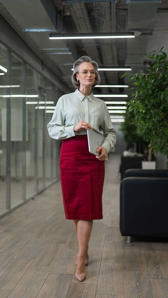 Attractive mature caucasian woman holding laptop while standing in office - Φωτογραφία, εικόνα
