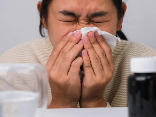 Niezdrowa Azjatka w swetrze dmuchająca nos w jednorazową tkankę. Alergia na kurz, sierść zwierzęcą, przeziębienie lub infekcję wirusową. Koncepcja zdrowia i medycyny. - Zdjęcie, obraz